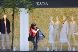 Mulher passa em frente à vitrine de uma loja Zara carregando sacolas da marca