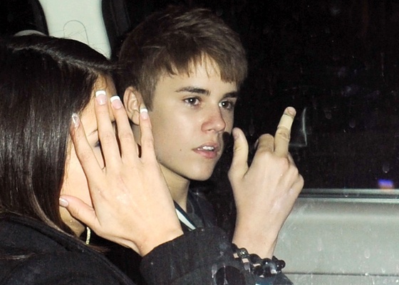 Justin Bieber mostra o dedo mdio ao lado da atriz Selena Gomez, que esconde o rosto, na sada de seu aniversrio em restaurante de Los Angeles (1/3/2011)